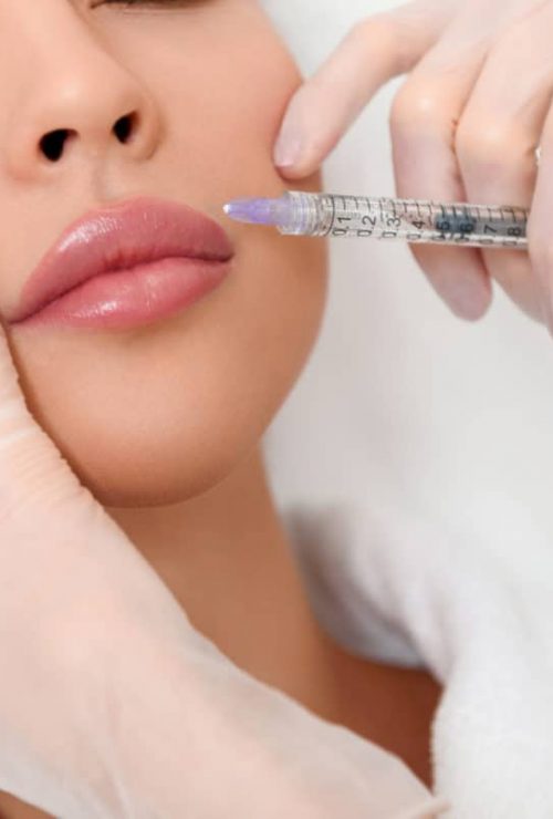 Close up of beautician hands in gloves injecting female lips with botox. Calm woman is lying with closed eyes